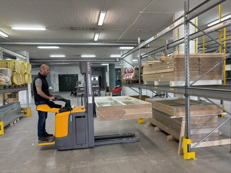 En truckförare lastar glaspartier i hyllsystem på lager.